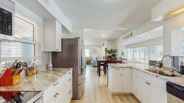 A modern kitchen with white cabinetry, a stainless steel refrigerator, and a marble countertop. - Waterfront home with private, heating optional pool, lanai, and internet (Bradenton)