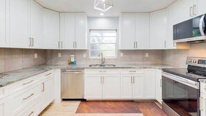 Una cucina moderna con mobili bianchi, lavastoviglie integrata, microonde e piano cottura.