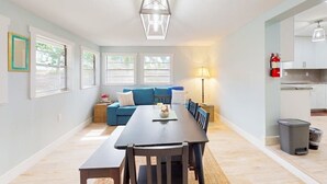 Un ambiente moderno con angolo pranzo, divano, lampada e zona cucina con pensili ed estintore.