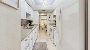 Una cocina estrecha con armarios blancos, salpicadero de azulejos y horno empotrado.