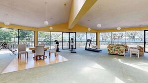 Una habitación amplia con ventanas grandes, una esterilla de yoga, equipo de ejercicio y un sofá.