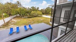 Ein Pool mit blauen Liegestühlen, Blick auf einen Garten mit Bäumen und ein Haus mit einer überdachten Veranda.