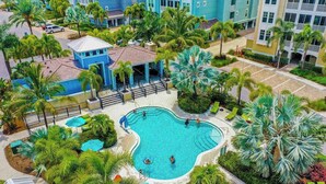 Piscina rodeada por palmeiras e um edifício com fachada azul.