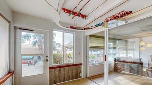 A room with a sliding glass door, a wooden bench, a bed with a metal frame, and a view of palm trees outside. - Waterfront Home with  Pool, Private Washer & Dryer, and Gazebo (Bradenton)