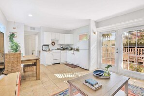Una cocina moderna con armarios blancos, un comedor con mesa y sillas, y vistas a través de un ventanal.
