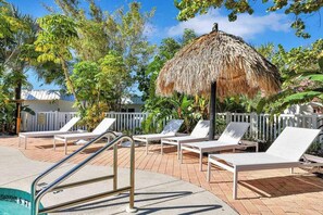A pool area with lounge chairs and a thatched umbrella.