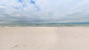Ein Strand mit weitem Sandufer und ruhiger See unter einem bewölkten Himmel.