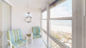 Ein Zimmer mit großem Fenster, zwei gestreiften Stühlen, einem kleinen Tisch und einer Wanduhr.