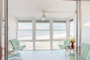 A room with large windows, a ceiling fan, and striped chairs. - Ocean-front condo with WiFi, pool & Gulf views - steps to the beach (Holmes Beach)