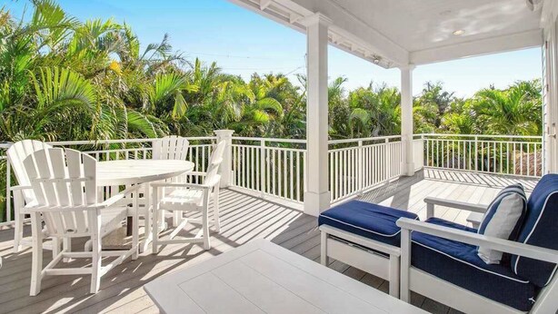 Eine überdachte Terrasse im Freien mit weißen Möbeln, darunter ein Tisch, Stühle und eine Couch mit blauen Kissen.