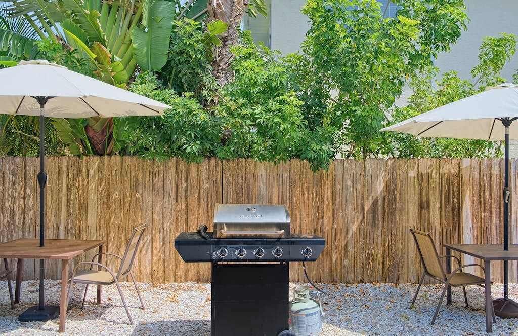 Un patio al aire libre con una parrilla, dos sombrillas y una valla de madera.