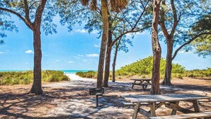 Un espace de pique-nique aménagé au bord de la plage, avec des bancs et une table à pique-nique, entouré d’arbres et donnant sur l’océan.
