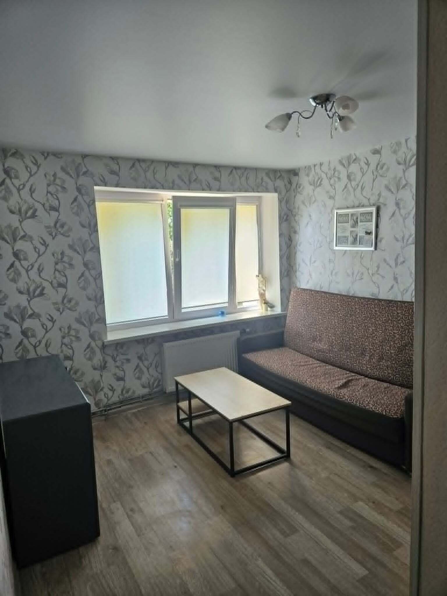 Une pièce comprenant un canapé, une petite table, un radiateur, une fenêtre à vitres dépolies et un ventilateur de plafond.
