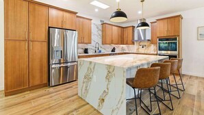 Une cuisine moderne avec des meubles en bois, des appareils en acier inoxydable, un îlot en marbre et des tabourets de bar.