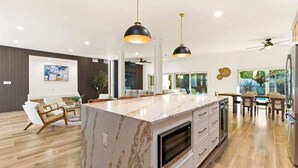 Une cuisine moderne dotée d’un îlot en marbre, de luminaires suspendus et d’un coin repas offrant une vue agréable.
