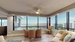 Un salon spacieux avec un balcon, de grandes fenêtres et un ventilateur de plafond.