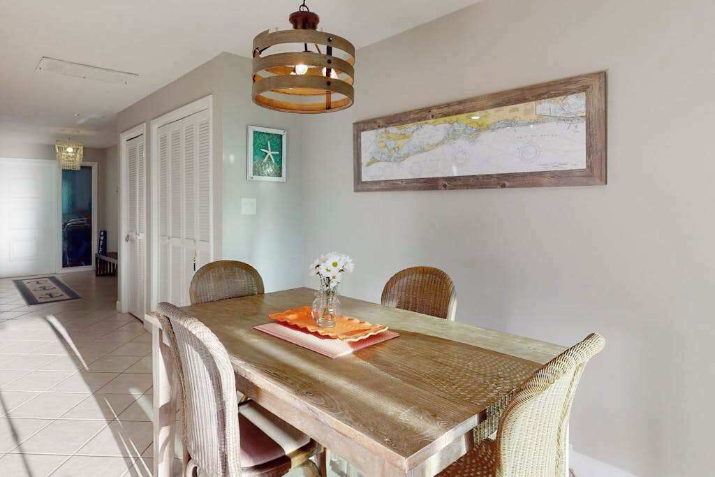 A dining area with a wooden table, wicker chairs, a hanging light fixture, and a framed map on the wall.