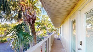 A covered corridor with a palm tree, a parked car, and a building with a green door. - Waterfront condo with Gulf views, pool, tennis, & deeded beach access (Longboat Key)
