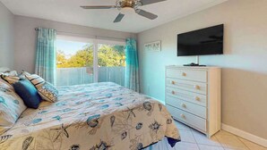 A bedroom with a bed, a ceiling fan, a TV, a dresser, and a view through a window. - Waterfront condo with Gulf views, pool, tennis, & deeded beach access (Longboat Key)