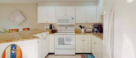 A compact kitchen with white cabinets, a microwave, stove, and a coffee maker.