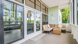 Un espace extérieur aménagé, abrité, avec un canapé et une table, une porte-fenêtre coulissante donnant sur un balcon, et une vue sur la verdure environnante.