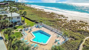 A pool area with a clear view of the ocean and beach, surrounded by greenery and a fenced pool. - Beachfront Condo with a Beautiful, Renovated Kitchen, Shared Pool, & Tennis (Longboat Key)