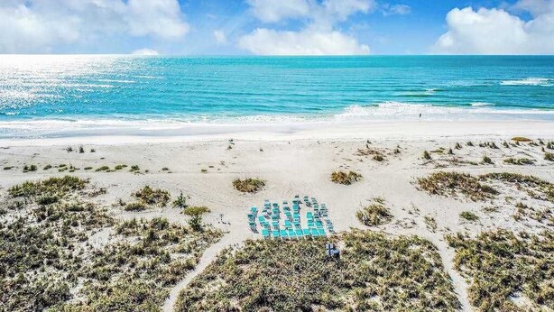 A beach with a clear view of the ocean, a sandy area with some vegetation, and a person standing near the water. - Beachfront Condo with a Beautiful, Renovated Kitchen, Shared Pool, & Tennis (Longboat Key)