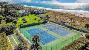 A tennis court surrounded by greenery and a beach view. - Beachfront Condo with a Beautiful, Renovated Kitchen, Shared Pool, & Tennis (Longboat Key)