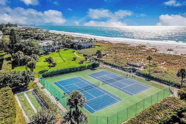 A tennis court surrounded by greenery and a beach view. - Beachfront Condo with a Beautiful, Renovated Kitchen, Shared Pool, & Tennis (Longboat Key)
