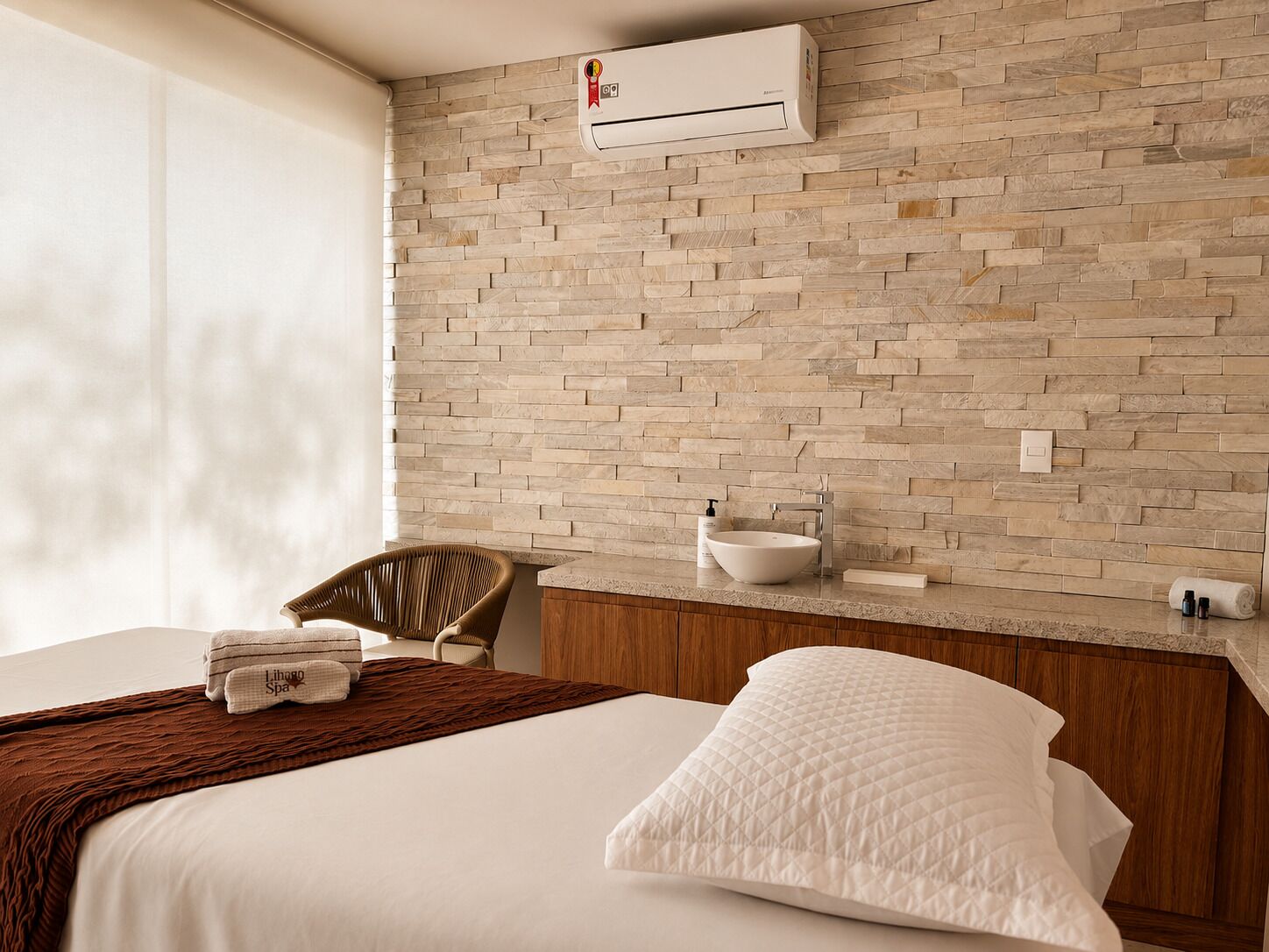Ett hotellrum med en vägg som har ett mönster av tegelstenar, en säng med vita sängkläder, en sänggavel i trä, ett badrum med handfat och hygienartiklar samt en luftkonditioneringsanläggning.