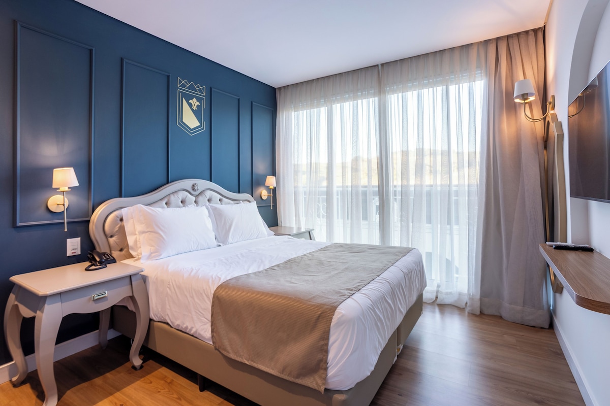 Una habitación de hotel con una cama grande, mesitas de noche, un televisor y una ventana con cortinas.