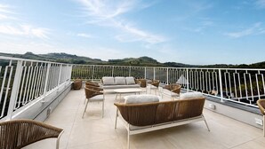 A balcony with wicker furniture, a white railing, and a view of green hills. - Castelos do Vale by Livá OFICIAL (Vale dos Vinhedos)