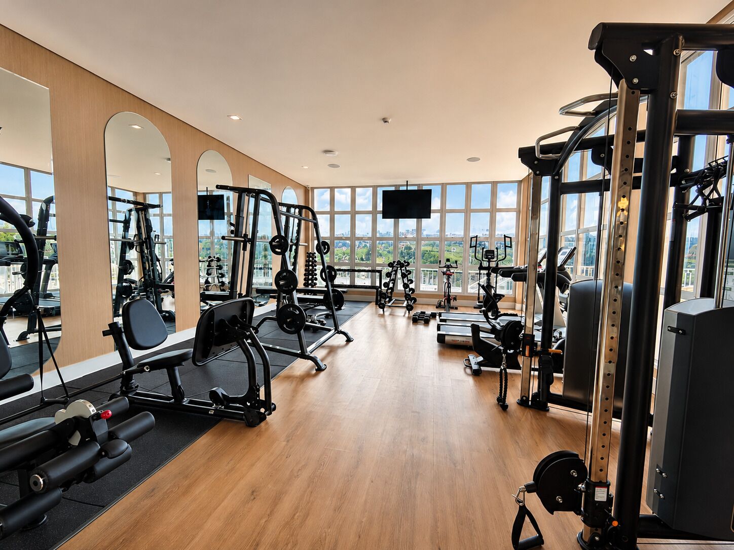 Ett gym med olika typer av träningsutrustning, stora fönster och en platt-TV.