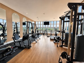 Un gimnasio con diverso equipo de ejercicio, ventanas amplias y un televisor de pantalla plana.