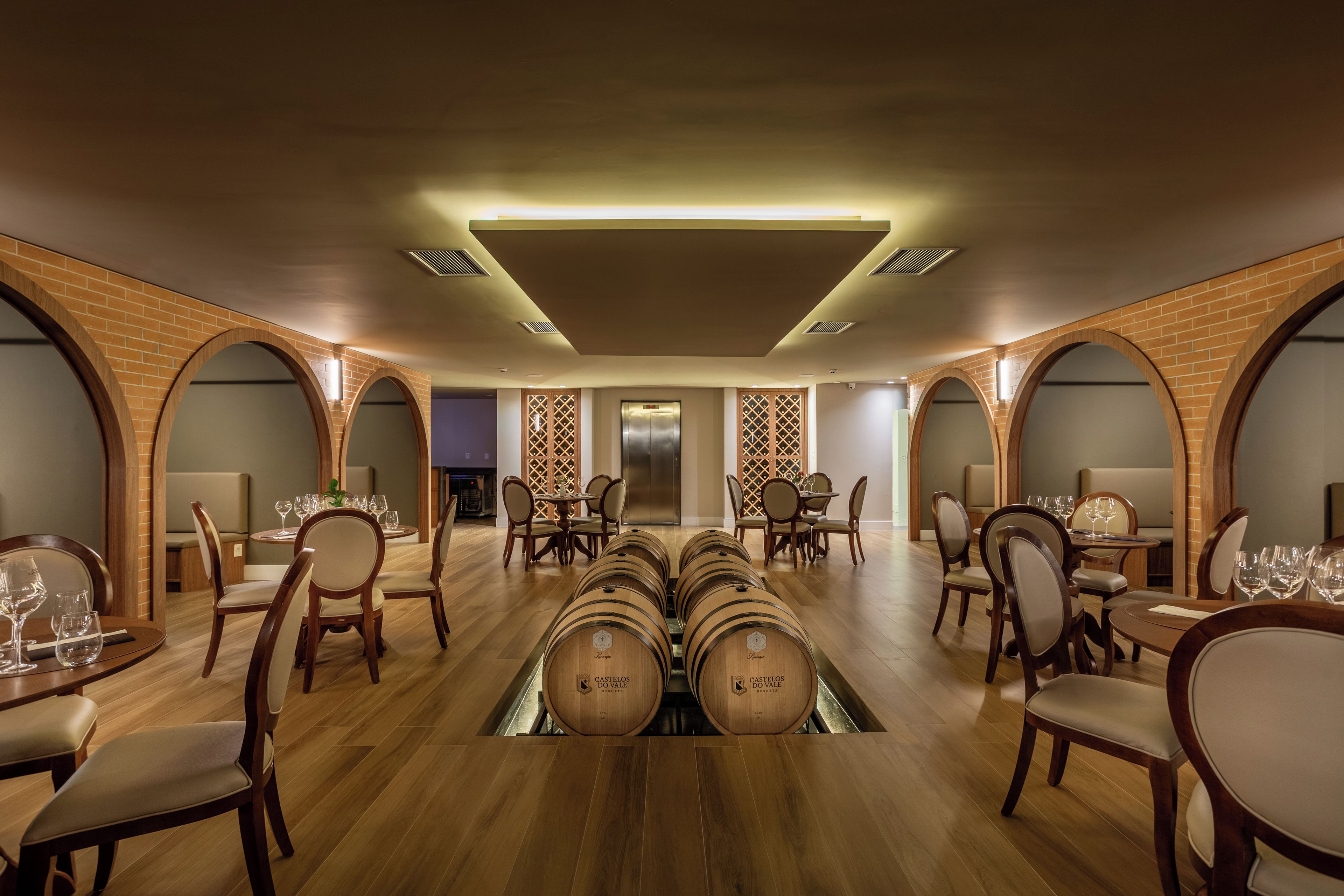 Restaurante com várias mesas, cadeiras e um mostruário de barris de vinho.