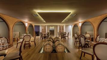 Restaurante com várias mesas, cadeiras e um mostruário de barris de vinho.