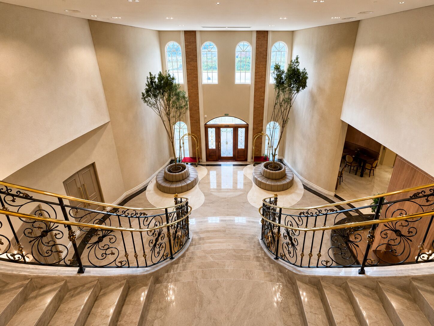 A grand hotel lobby with a marble staircase, a central seating area, and large arched windows.