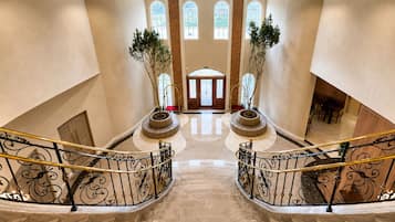 A grand hotel lobby with a marble staircase, a central seating area, and large arched windows.