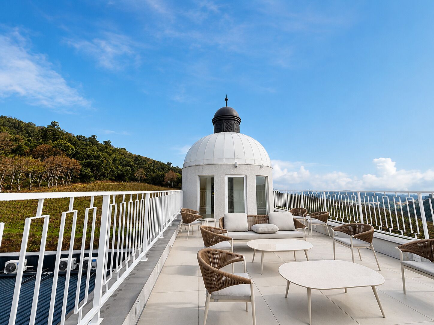 A rooftop terrace with a white dome structure, wicker furniture, and a white railing.