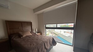 A bedroom with a large bed, a nightstand, a window with a view of a swimming pool, and a balcony. - Duo 24 Apartment, Tower A (Zapopan)