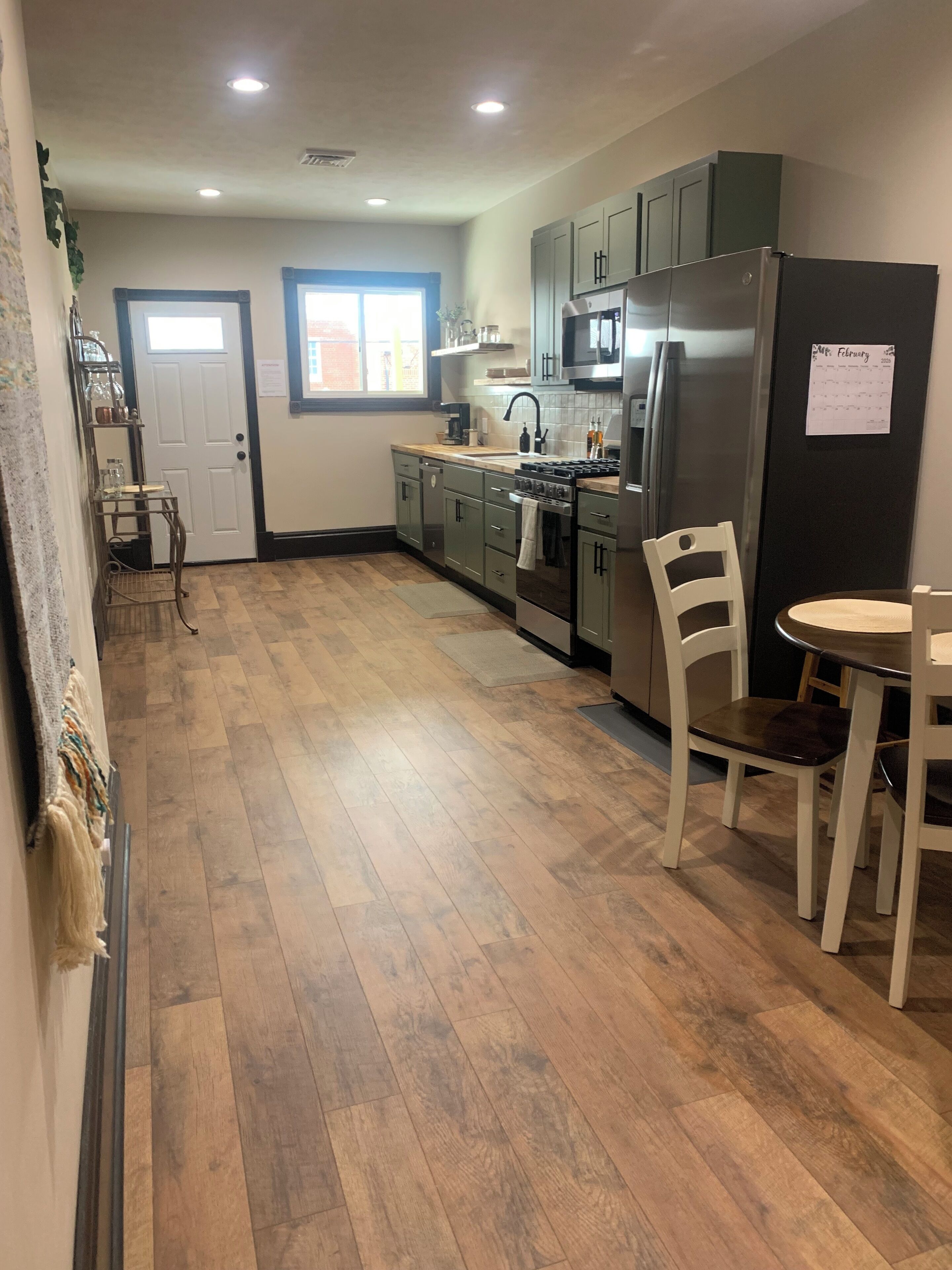 A kitchen with wooden flooring, a refrigerator, cabinets, a stove, and a dining table with chairs.