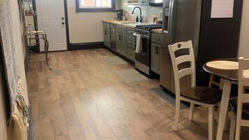 A kitchen with wooden flooring, a refrigerator, cabinets, a stove, and a dining table with chairs.