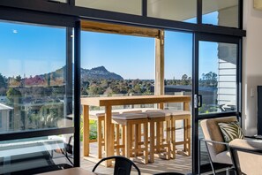 Ein Balkon mit Holztisch und Stühlen, großen Fenstern und Blick auf eine Hügelkuppe.