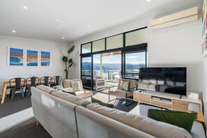 Ein modernes Wohnzimmer mit einer Couch, Sesseln, einem Fernseher und einem Essbereich mit Stühlen und einem Tisch.