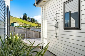 Ein Haus mit einer Terrasse, einem Fenster mit Dusche und Blick auf einen Hügel.