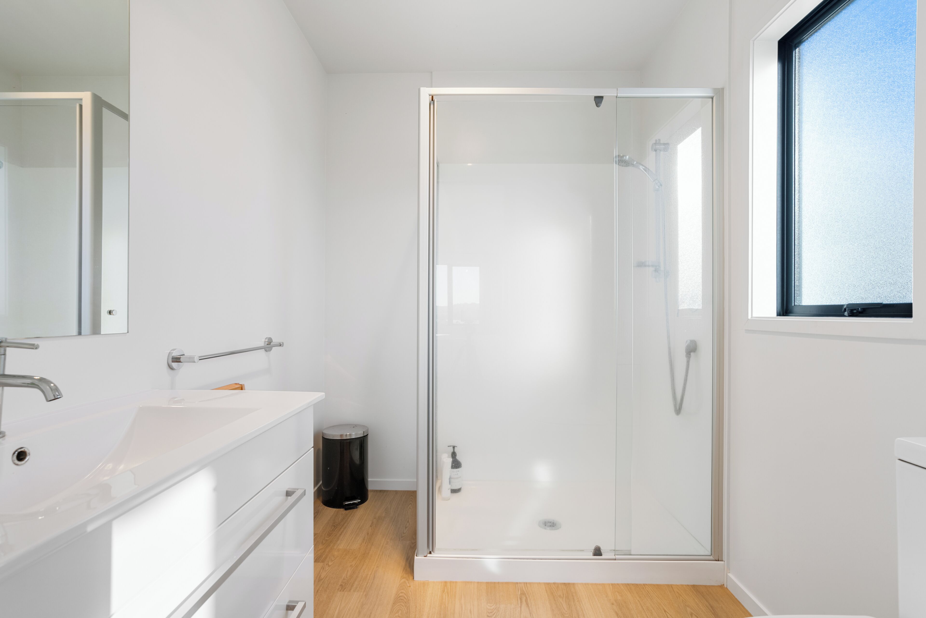 A modern bathroom with a glass-enclosed shower, a white sink, and a mirror.