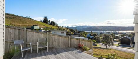Una terraza de madera con dos sillas, una cerca de madera y vista a un paisaje montañoso con edificios a lo lejos.