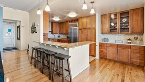 Eine moderne Küche mit Holzschränken, einer zentralen Kochinsel mit Hockern, Pendelleuchten und einem Edelstahl-Kühlschrank.