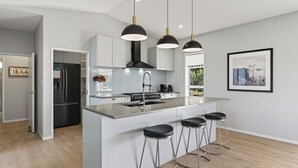 A modern kitchen with a central island, stainless steel appliances, pendant lighting, and a framed picture on the wall. - Meadow Escape - Mangawhai Holiday Home (Mangawhai)