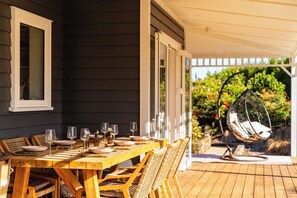 Una terraza de madera con una mesa lista para comer, sillas exteriores y una silla colgante.